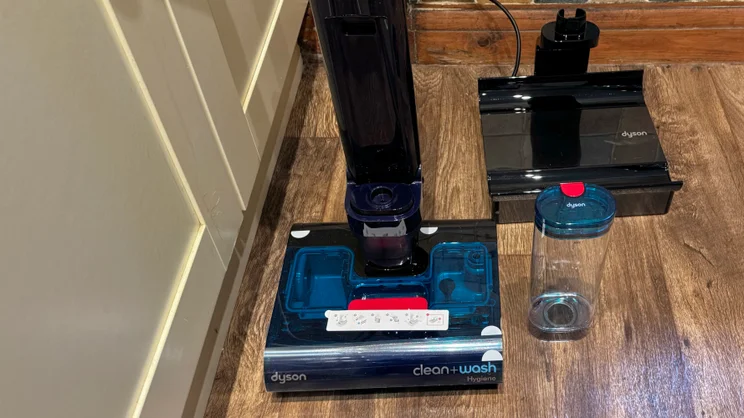 Dyson Clean and Wash Hygiene cleaner head with the clean water tank removed, standing beside the black dock tray and the detached tank