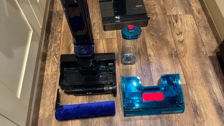 Dyson Clean and Wash Hygiene taken apart on the floor, showing the removed blue cover, the black head with roller bar, the blue microfibre roller and the water tank