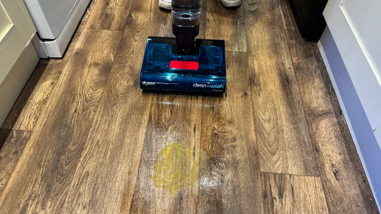 Dyson Clean and Wash Hygiene cleaner head on wood-effect flooring, with a mustard spill and a wet streak left behind on the floor