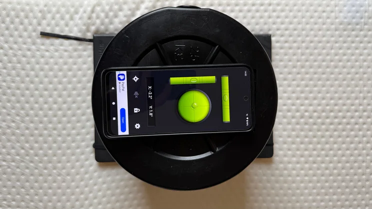 A bird's eye view of a smartphone and a stack of weights on top of the Emma Original mattress. A spirit level app is being used to measure tilt at the edge of the mattress