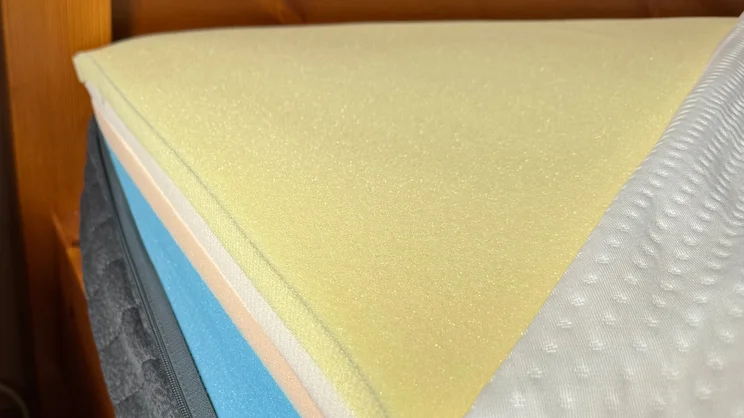 A corner of the Emma Original mattress with the cover partially removed, revealing its exposed memory foam layers underneath