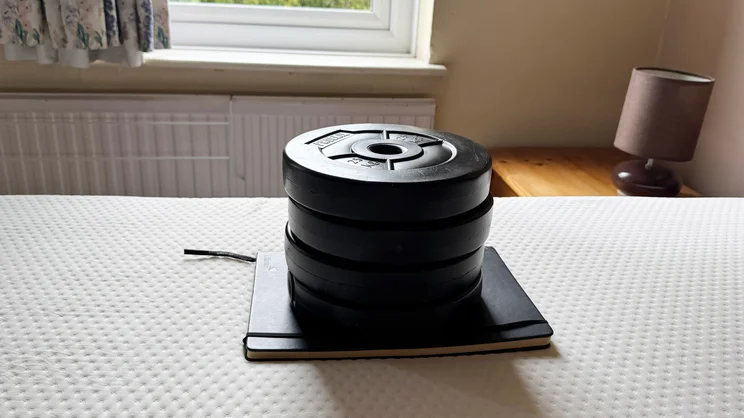 A notebook and a stack of weights on top of the surface of the Emma Original mattress