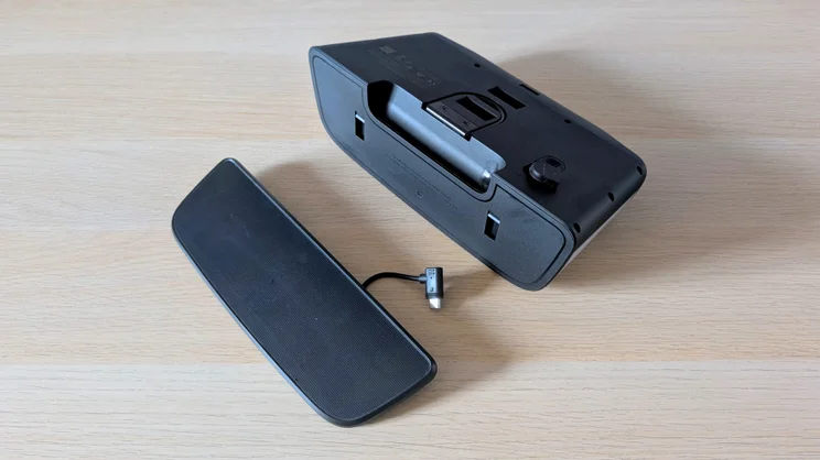 Rear of the Eufy S4 4K Solar Wall Light with its detachable black solar panel unclipped and lying beside it, the panel's short cable ending in an angled USB-C plug.