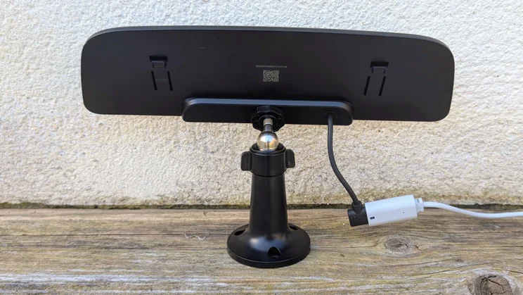 Back of the Eufy S4 4K Solar Wall Light's solar panel on an adjustable black ball-joint mount, standing on a wooden ledge against a white wall with its cable and white extension connector attached.