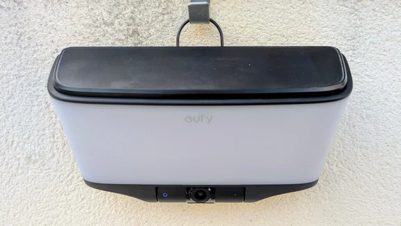 Front view of the Eufy S4 4K Solar Wall Light mounted on a wall with the solar panel clipped on top, the eufy logo on the frosted panel and the camera with a blue indicator ring below.