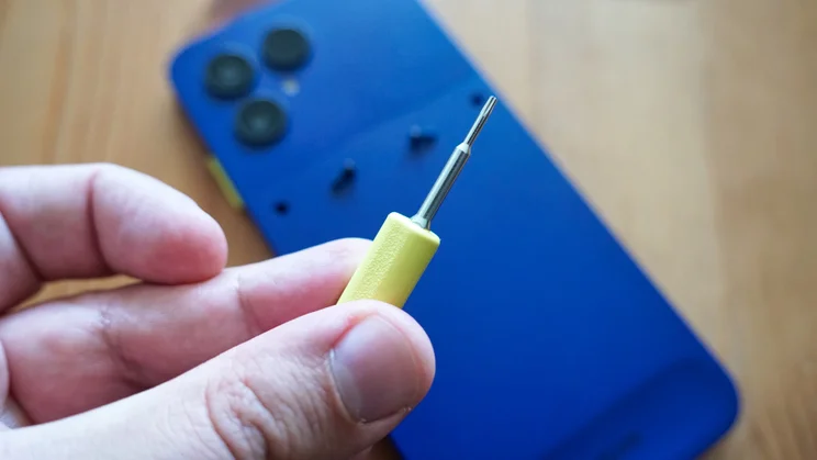 Hand holding tiny screwdriver over the Fairphone 6 Plus