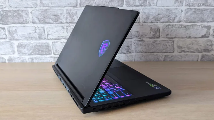 Rear three-quarter view of the MSI Raider 16 HX with the lid raised, showing the glowing MSI dragon shield logo on the lid and the RGB keyboard