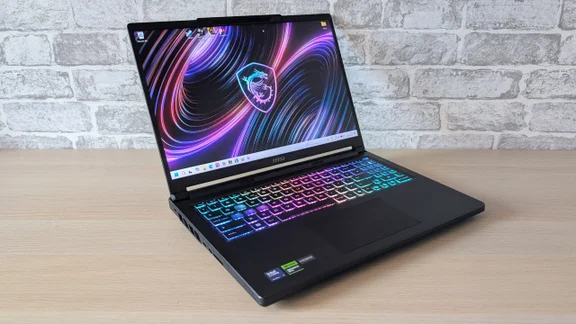 MSI Raider 16 HX gaming laptop open on a wooden desk, with a purple MSI dragon wallpaper on screen and a rainbow RGB backlit keyboard