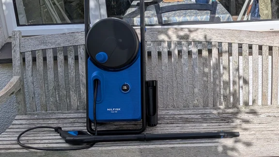 Front view of the Nilfisk Core 150 PowerControl on a wooden garden bench, with the hose reel on top, the Power Control dial and the trigger gun and lance in front.