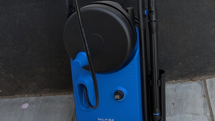 Close-up of the Nilfisk Core 150 PowerControl hose reel and Power Control dial, with the high-pressure hose looped across the front and the lance stored at the side.