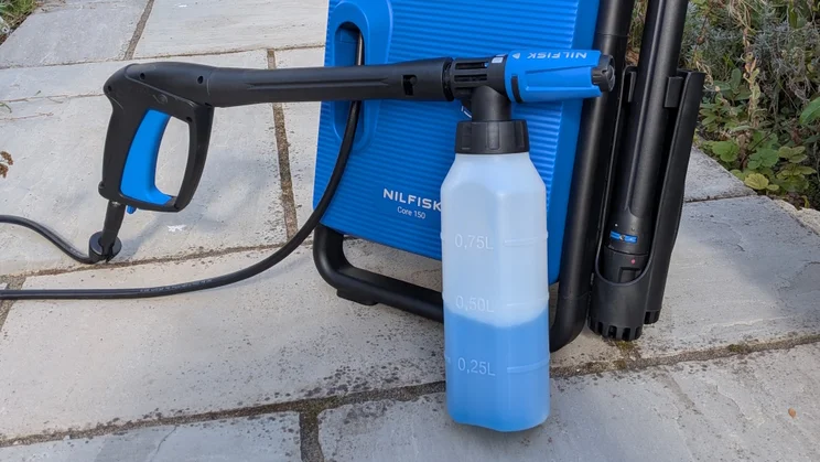 Nilfisk foam bottle with a blue detergent mix attached to the trigger gun of the Nilfisk Core 150 PowerControl, with litre markings from 0.25L to 0.75L.