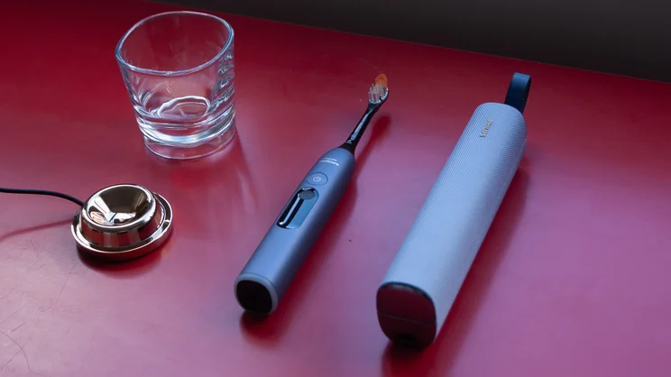 The Philips Sonicare DiamondClean 9900 Prestige electric toothbrush, alongside its attachments - including charging base, glass, and travel case - laying on a red table