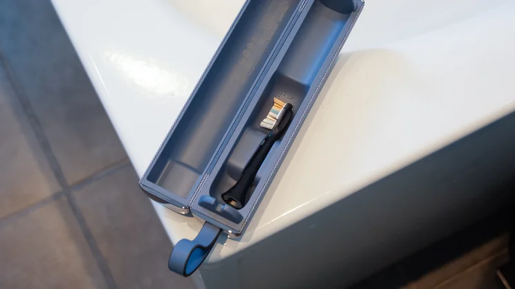 A bird's eye view of the Philips Sonicare DiamondClean 9900 Prestige electric toothbrush brush head in its travel case, on the corner of a bath tub