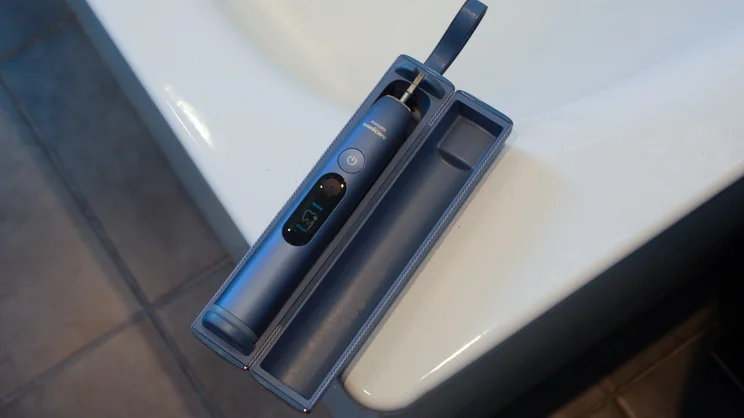 A bird's eye view of the Philips Sonicare DiamondClean 9900 Prestige electric toothbrush, head removed, in its open travel case on the corner of a bath tub