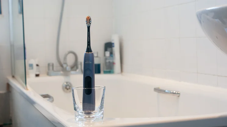The Philips Sonicare DiamondClean 9900 Prestige electric toothbrush standing upright on the corner of a bathtub