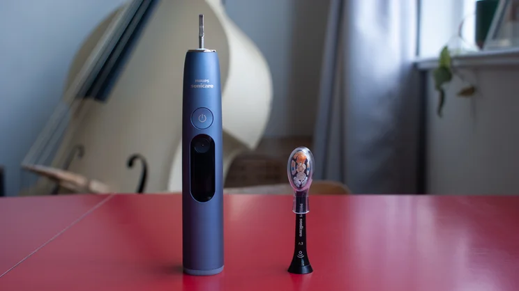 The Philips Sonicare DiamondClean 9900 Prestige electric toothbrush, with its removed brush head placed beside it, standing on a red table