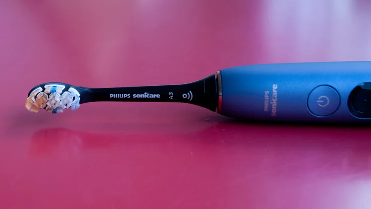 A closeup of the Philips Sonicare DiamondClean 9900 Prestige electric toothbrush's brush head, lying on its side on a red table