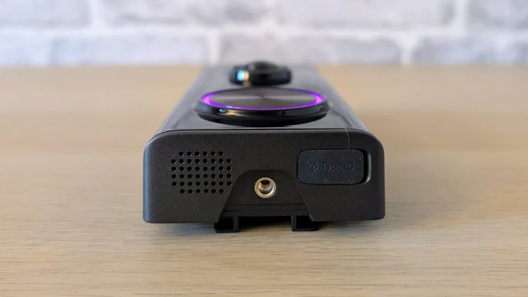 Bottom end of the Tapo D260 Pro doorbell showing the speaker grille, a threaded screw hole, a Type-C charging port cover and the purple-lit button ring beyond.