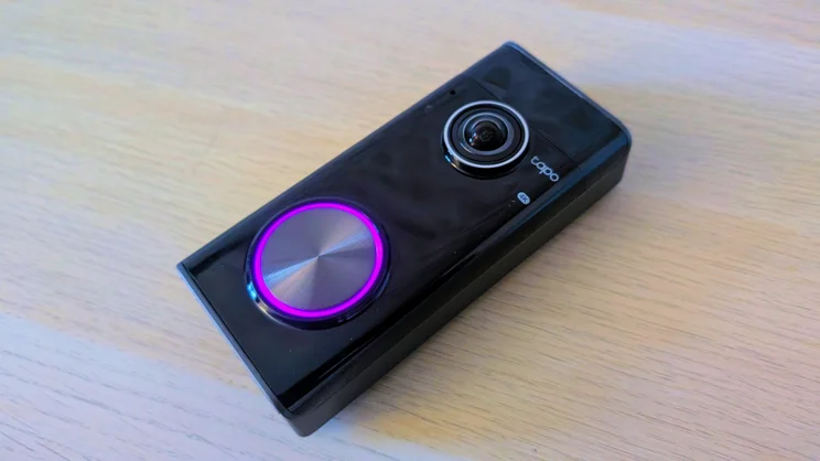 Tapo D260 Pro doorbell lying flat on a light wooden table at an angle, with the 4K camera lens at the top and a glowing purple ring around the button.