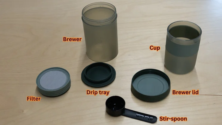 The Wacaco Prestina coffee maker, separated into its separated parts on an office table. Each part has been labelled