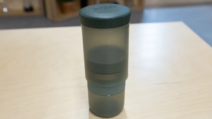 The Wacaco Prestina coffee maker, with lid attached, standing upright on an office table