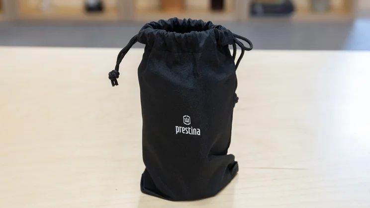 The Wacaco Prestina coffee maker in its drawstring travel bag, on an office table
