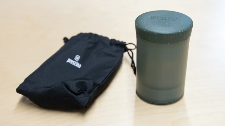 The Wacaco Prestina coffee maker, next to its drawstring bag, on an office table
