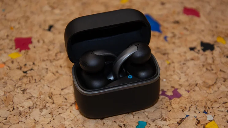The black charging case of the Anker Soundcore AeroClip 2 clip-on earbuds resting open on a textured cork surface, showing both buds docked in their moulded slots