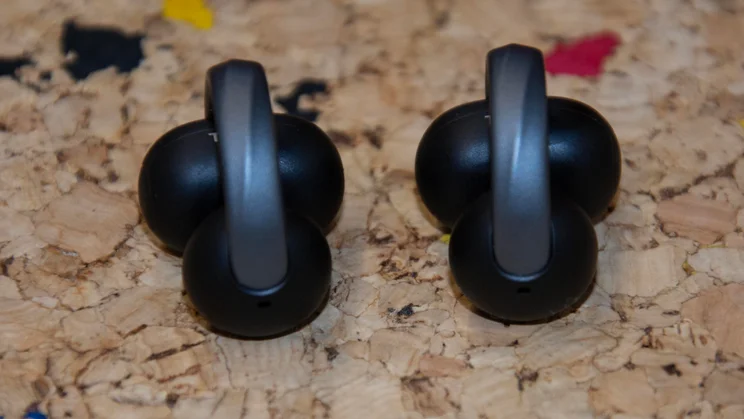 A pair of black Anker Soundcore AeroClip 2 clip-on earbuds lying flat on a cork surface, showcasing the curved connecting arches and dual-pod structure
