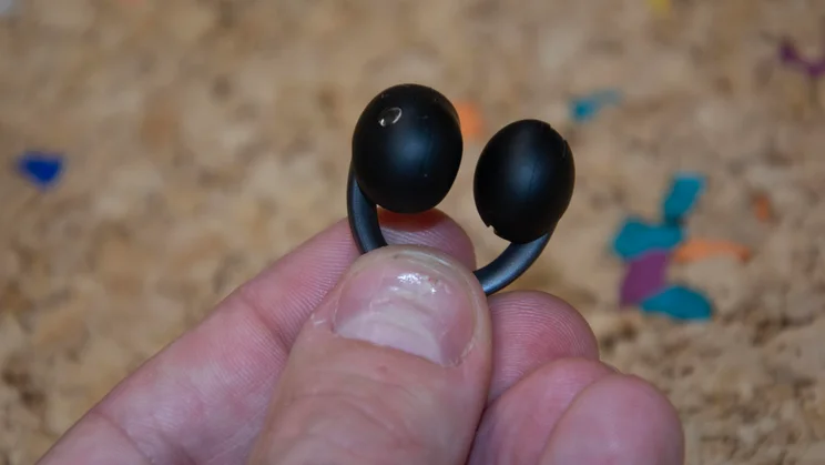 A close-up view of a hand holding an Anker Soundcore AeroClip 2 clip-on earbud, illustrating its flexible curved bridge design