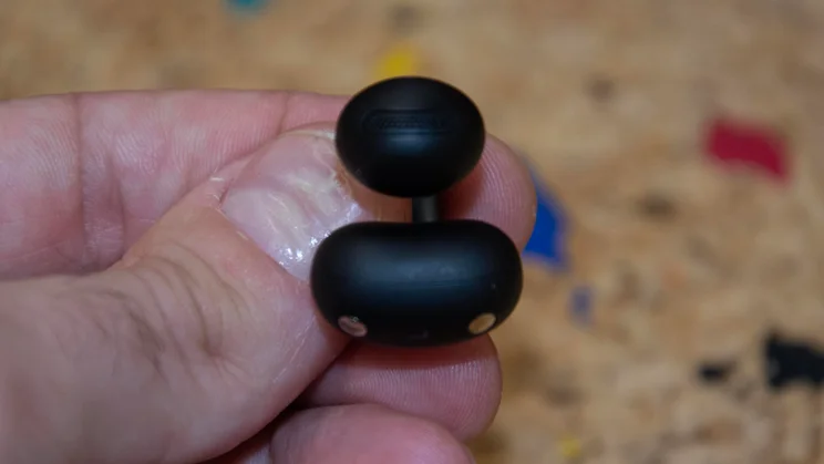 Close-up of a single black Anker Soundcore AeroClip 2 clip-on earbud held between fingers, showing the speaker grille and magnetic charging contacts