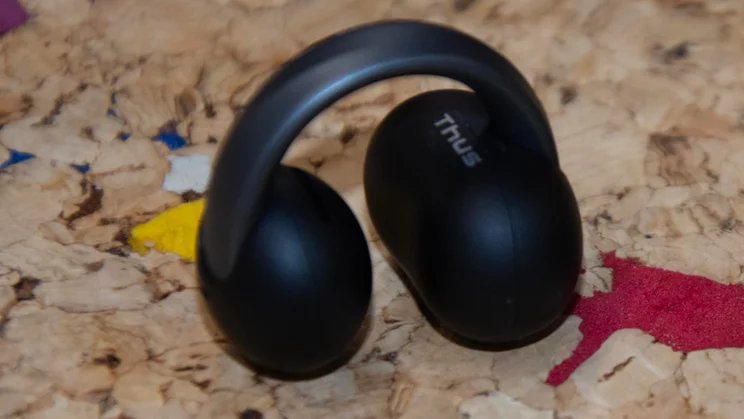A single black Anker Soundcore AeroClip 2 clip-on earbud resting upright on a cork surface, displaying the arched bridge connecting the two pods and subtle text branding on the inner casing