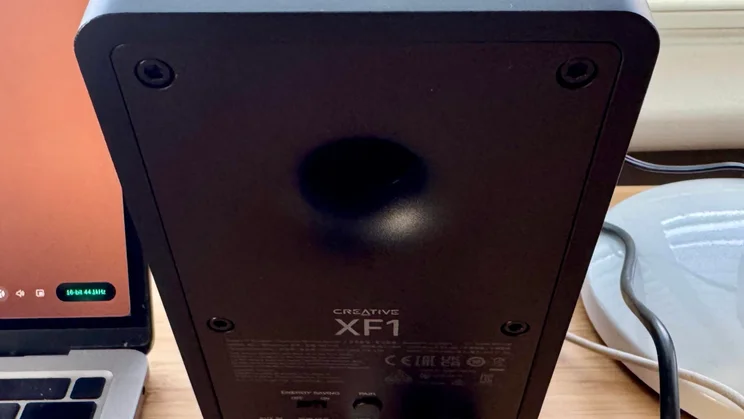 Rear view of a black Creative XF1 desktop speaker, featuring a circular bass reflex port, product labelling, and control switches
