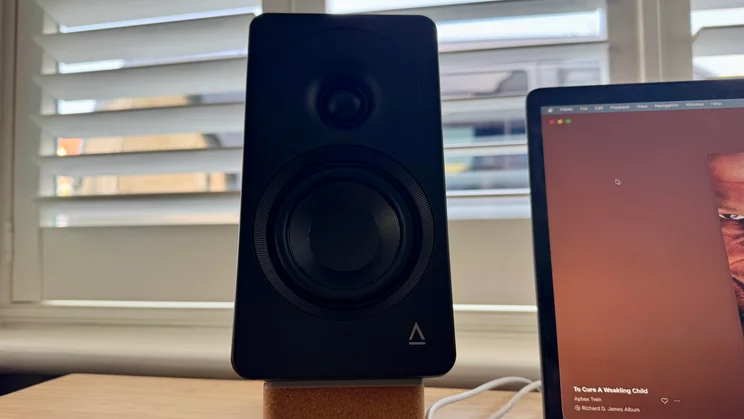 Front view of the left Creative XF1 desktop speaker resting on a cork stand, showing its tweeter, woofer driver, and the logo on the bottom right