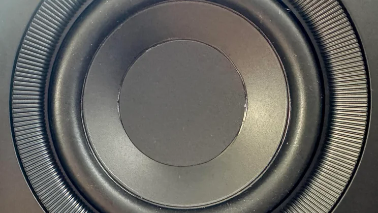 Extreme close-up shot of the mid-bass driver on a Creative XF1 desktop speaker, showing the ribbed surround texture and central cone