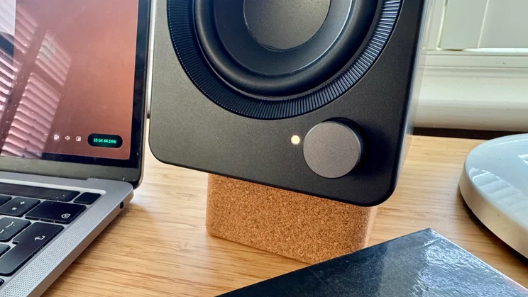 Close-up of the front bottom-right corner of the right Creative XF1 desktop speaker, showing the illuminated LED status indicator and rotary volume dial