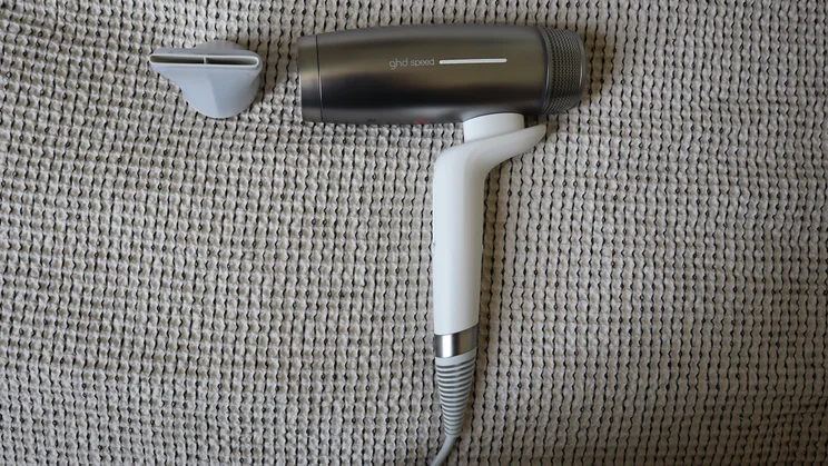 A bird's eye view of the GHD Speed Ionic hair dryer, on a grey blanket, alongside its concentrator nozzle