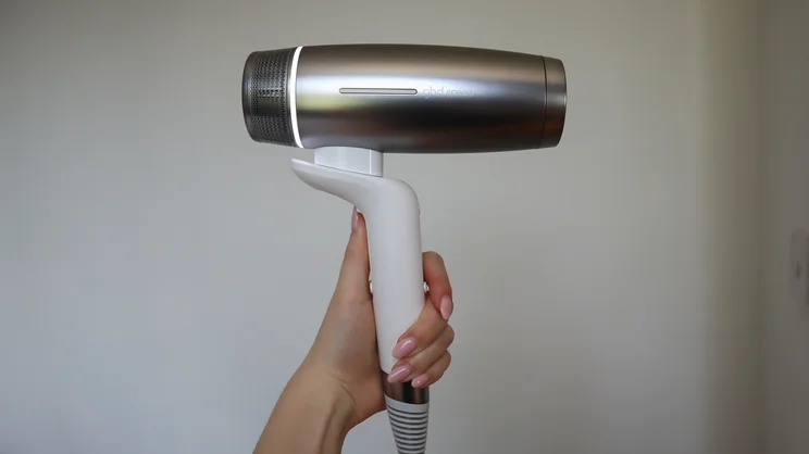 A hand holding up the GHD Speed Ionic hair dryer against a white wall background