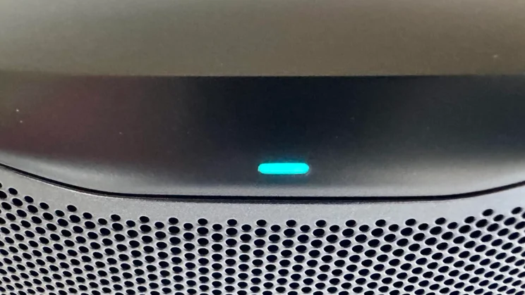 Close-up of the front rim of the JBL Cove M1 wireless speaker, showing a glowing cyan status indicator light above the speaker grille