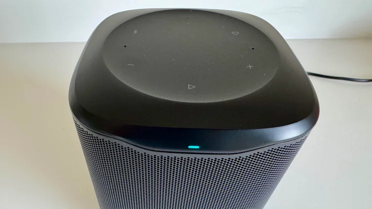 Elevated front view of the JBL Cove M1 wireless speaker, showing the illuminated status LED and the touch-sensitive control panel situated on the top surface