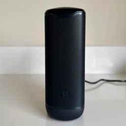 Front view of the black JBL Cove M1 wireless speaker standing upright on a counter, showing the wrap-around speaker grille with the JBL logo at the base
