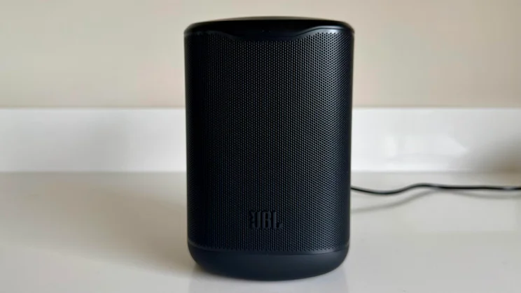 Front view of the black JBL Cove M1 wireless speaker standing upright on a counter, showing the wrap-around speaker grille with the JBL logo at the base