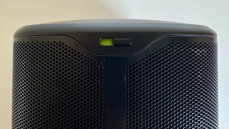 Close-up of the rear upper section of the JBL Cove M1 wireless speaker, showing the physical microphone mute switch toggled to reveal a green indicator