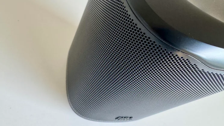 High-angle, close-up view focusing on the curved, perforated speaker grille wrapping around the body of the JBL Cove M1 wireless speaker