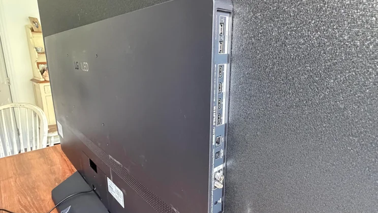 Side-angle view of the rear connectivity panel on the 77in LG C6 OLED featuring Primary RGB Tandem OLED technology, displaying stacked HDMI 2.1 ports, USB slots, an Ethernet (LAN) port, optical audio output, and antenna inputs on a dark textured cabinet