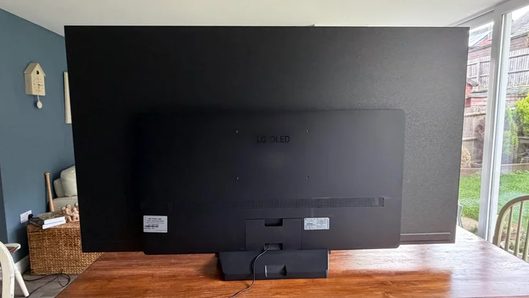 Full rear view of the 77in LG C6 OLED TV featuring Primary RGB Tandem OLED technology, showing the central mounting bump, base stand, cable management routing, and overall back panel construction