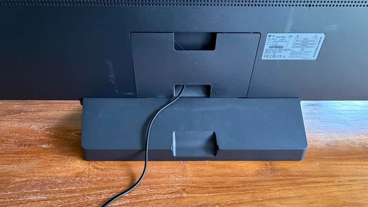 Rear close-up view of the pedestal stand base attached to the back panel of the 77in LG C6 OLED TV featuring Primary RGB Tandem OLED technology, demonstrating the cable routing path and rear cover plate