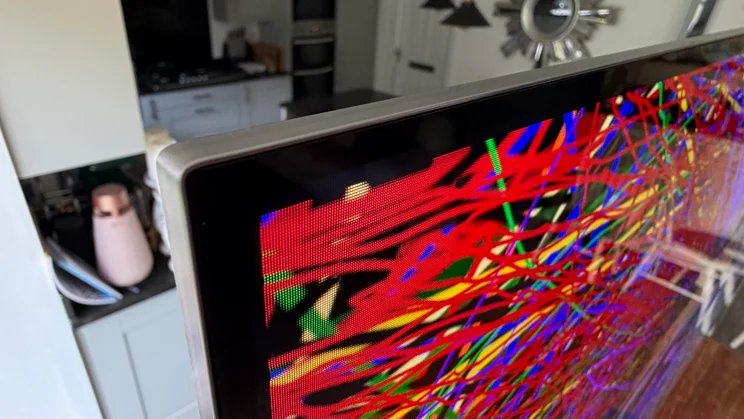 Close-up extreme angle of the top-left corner frame and screen boundary of the 77in LG C6 OLED TV with Primary RGB Tandem OLED technology, showing the slim metallic bezel and detailed sub-pixel structure displaying bright red and green lines