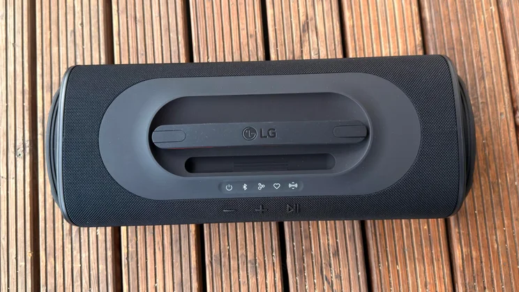 A top-down perspective of the LG xboom Blast portable speaker resting on wooden slats, clearly showing the integrated top carrying handle with LG branding, control status icons, and playback buttons
