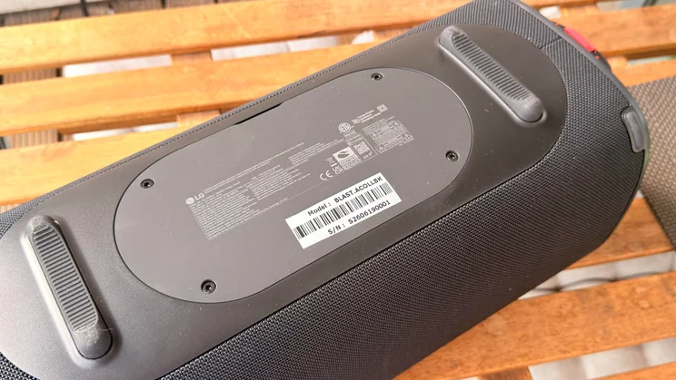 A view of the underside of the LG xboom Blast speaker resting on a wooden surface, showing two rubber stabilising feet and the central product information label with model number and serial number details